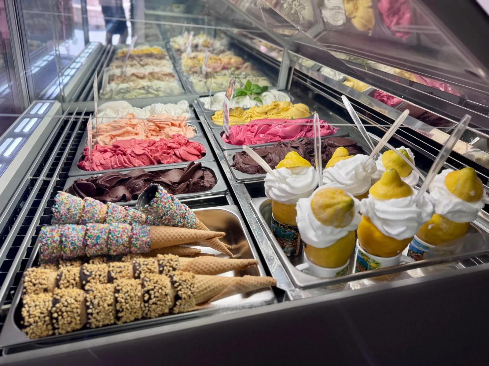 Vetrina di gelateria con vaschette di gelato, coni decorati e limoni ripieni