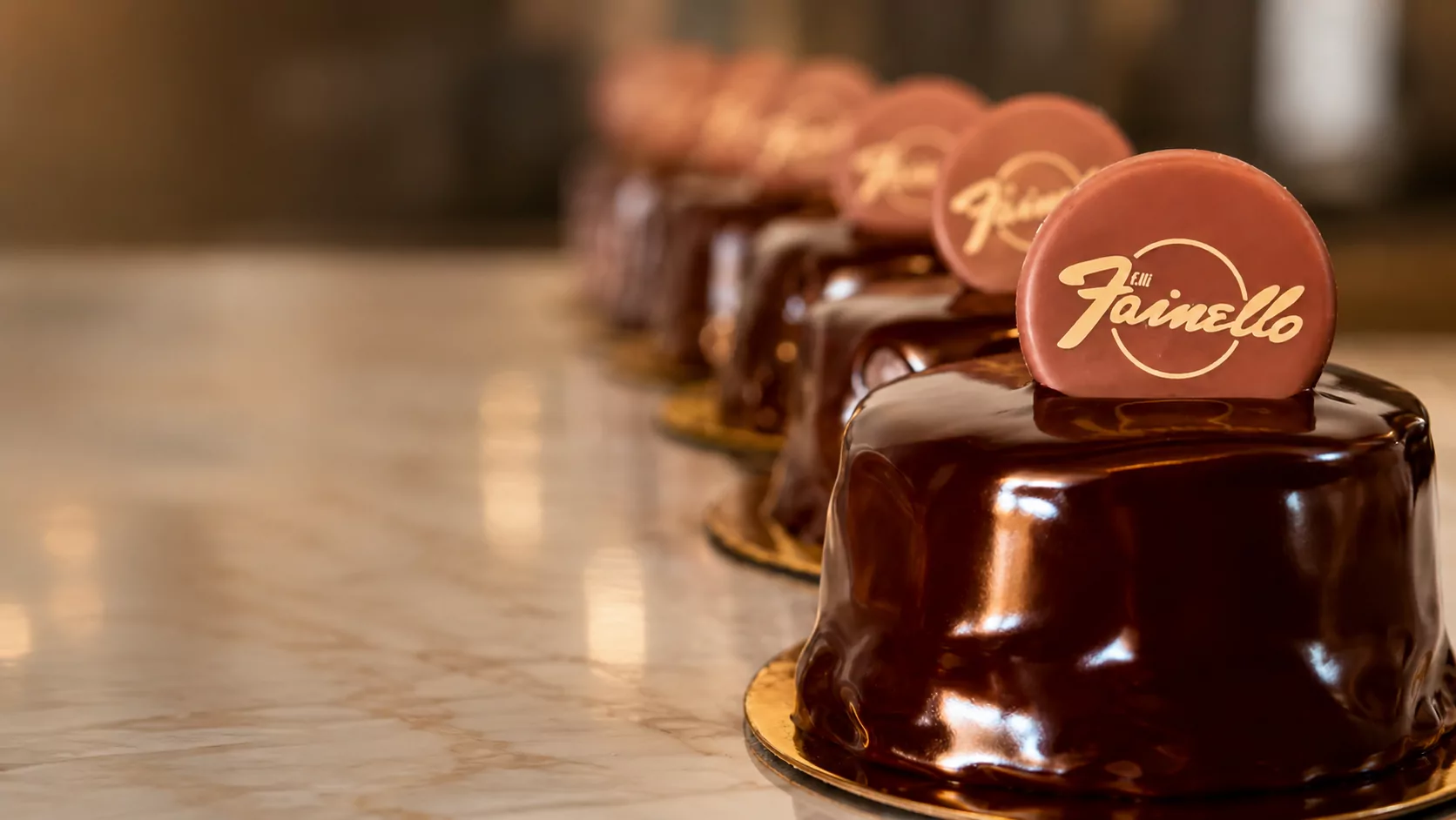 Fila di monoporzioni glassate al cioccolato fondente, ciascuna con un disco di cioccolato ruby inciso in oro con il logo f.lli Fainello
