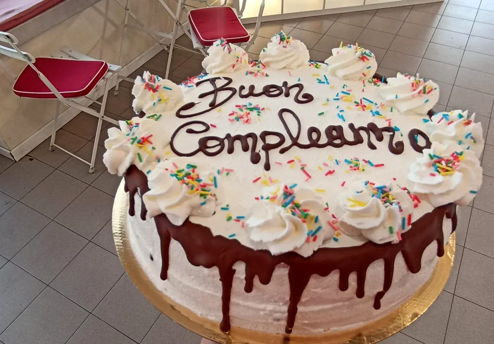 Torta di compleanno con panna, colata di cioccolato e zuccherini colorati